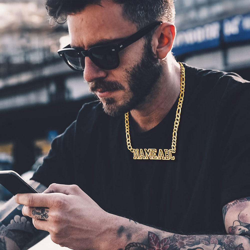 Man wearing sunglasses and a gold chain necklace with 'NAME ALEC' text, using a phone.