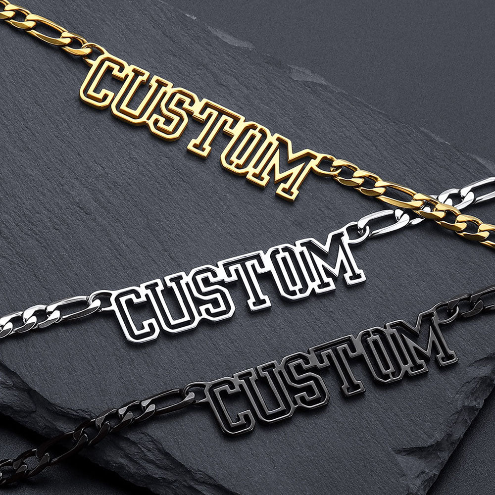 Three gold, silver, and black 'CUSTOM' chain necklaces on a dark surface.