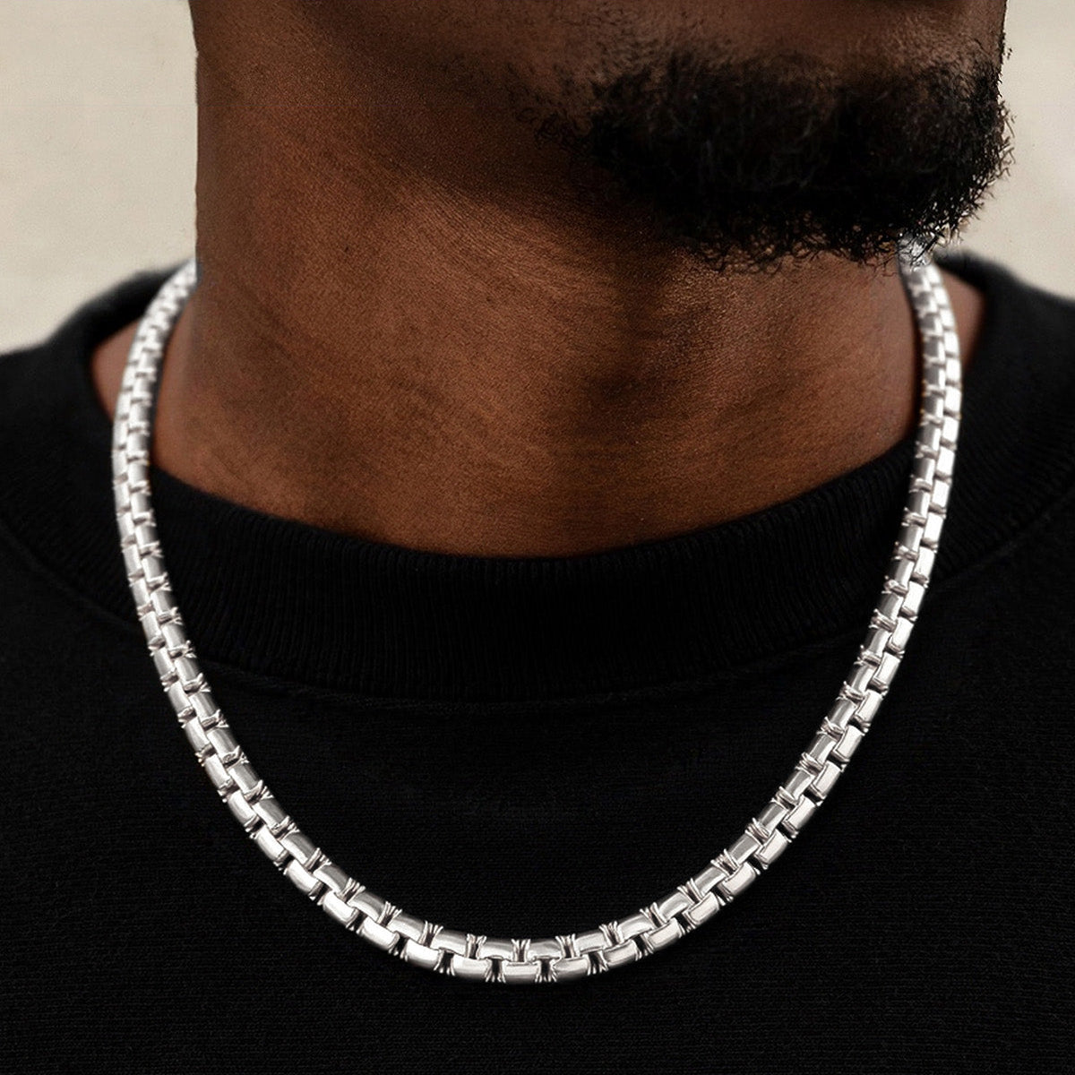 Silver chain necklace worn by a person on a black background