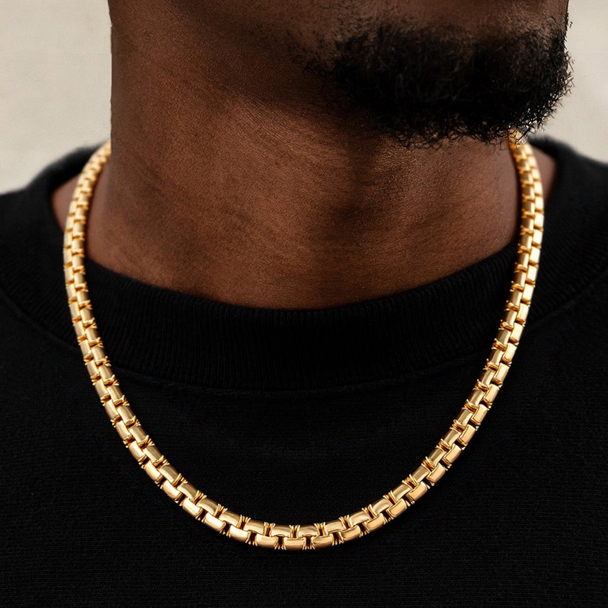 Gold chain necklace worn by a person on a black background