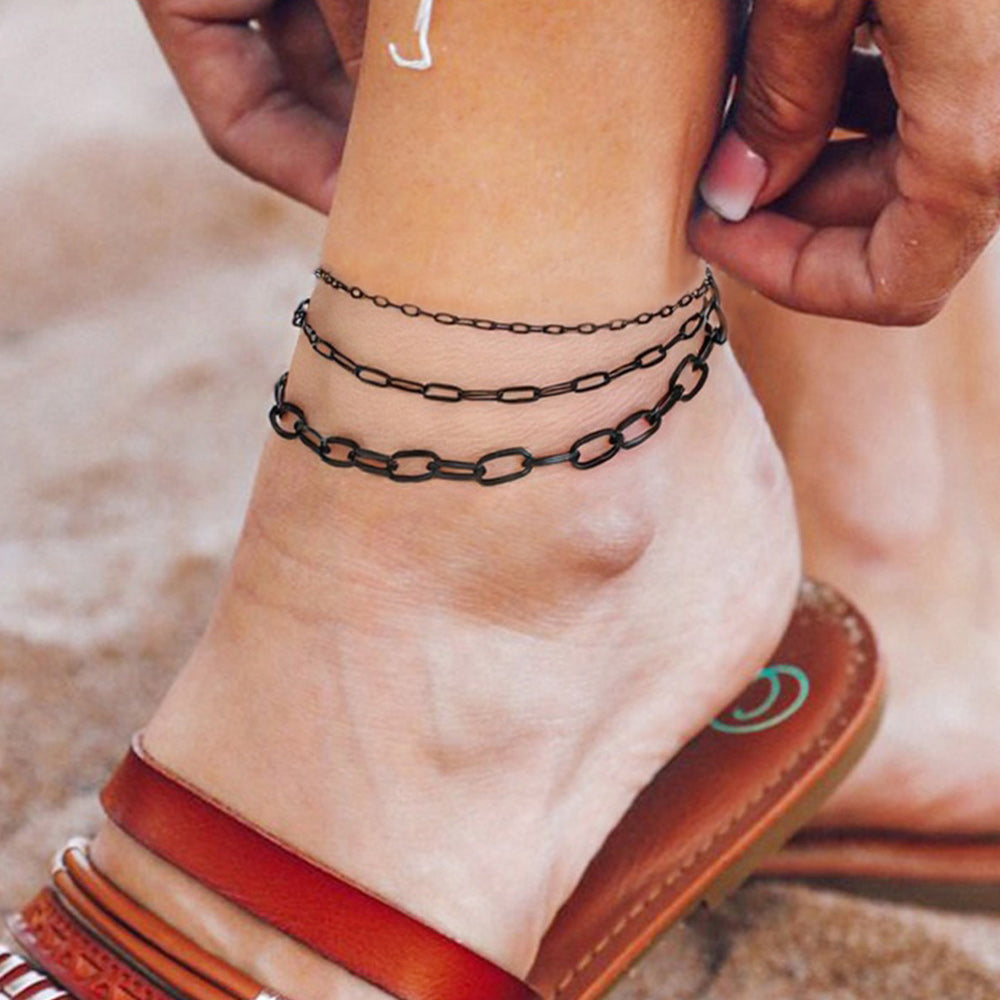 Woman showing 2mm, 3mm, and 6mm widths black paperclip anklet at the beach