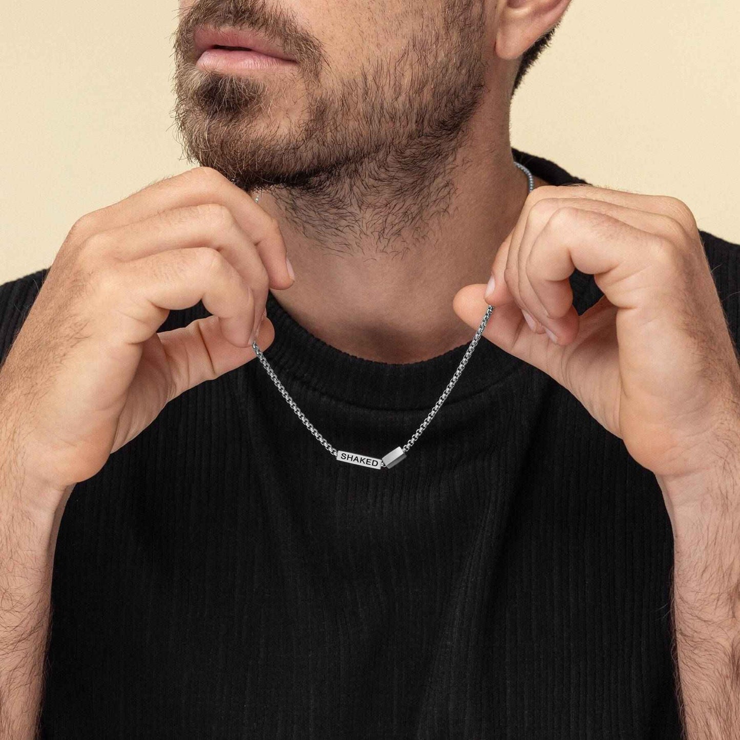 Man adjusting a silver necklace with a pendant on a beige background