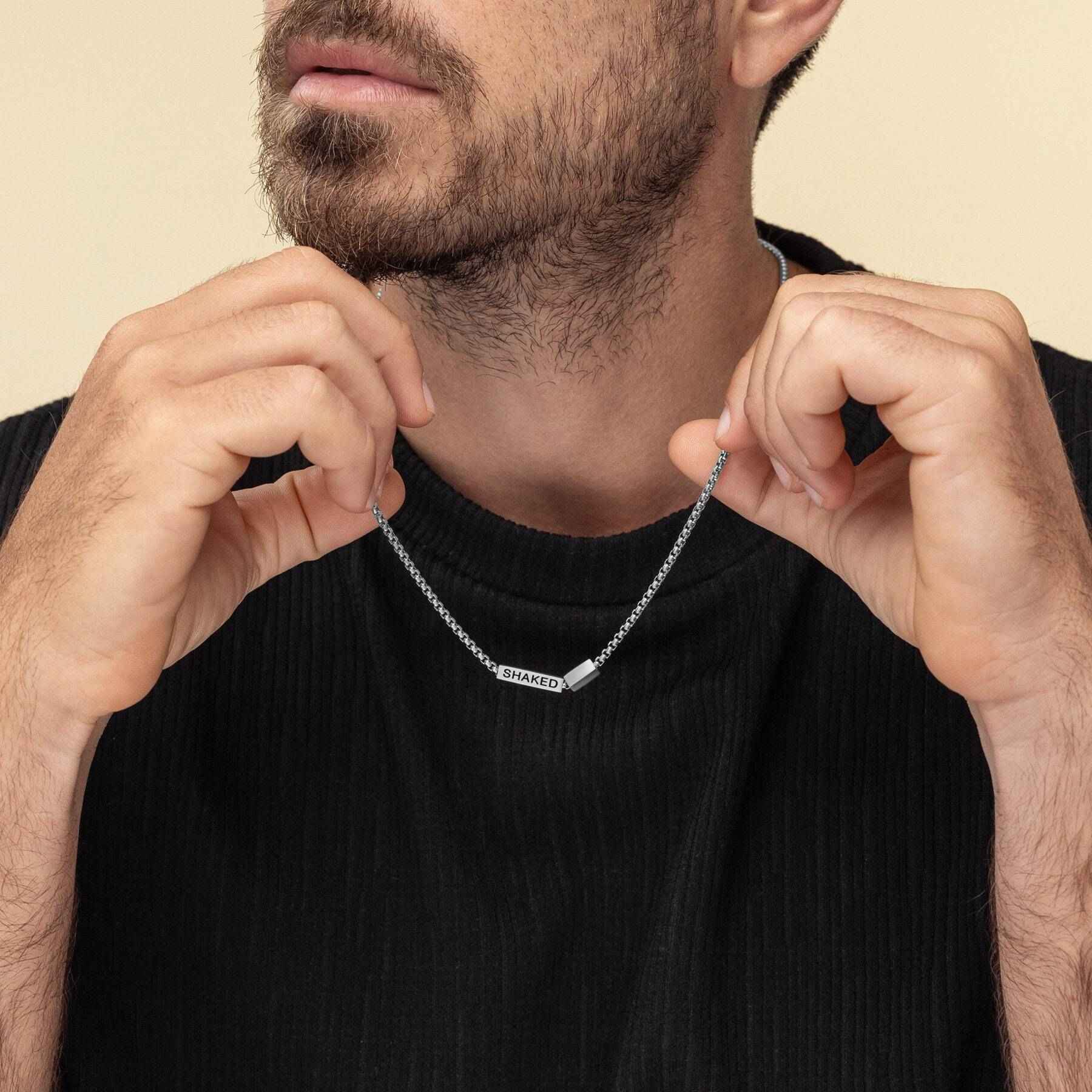 Man adjusting a silver necklace with a pendant on a beige background