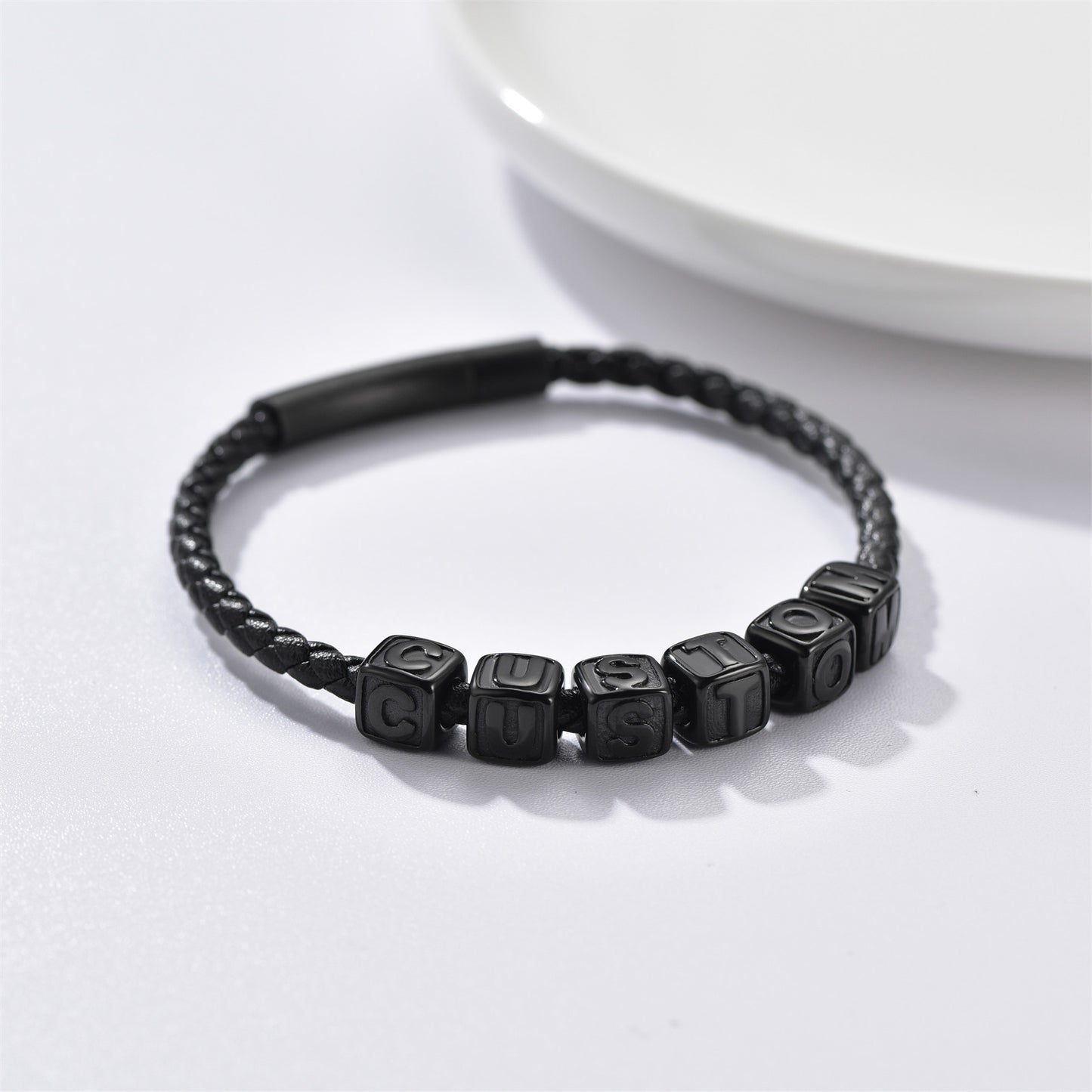 Black braided bracelet with lettered beads on a white background