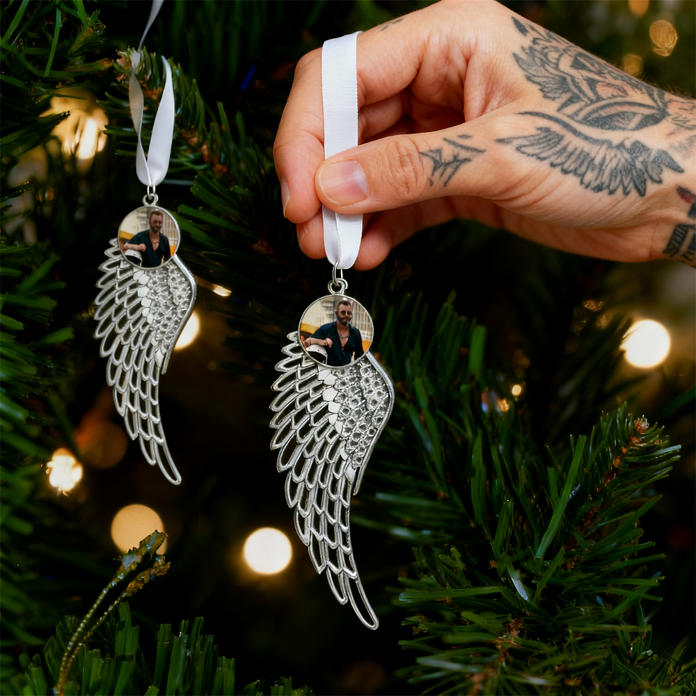 Silver angel wing ornament with a photo charm held by a hand against a Christmas tree background.