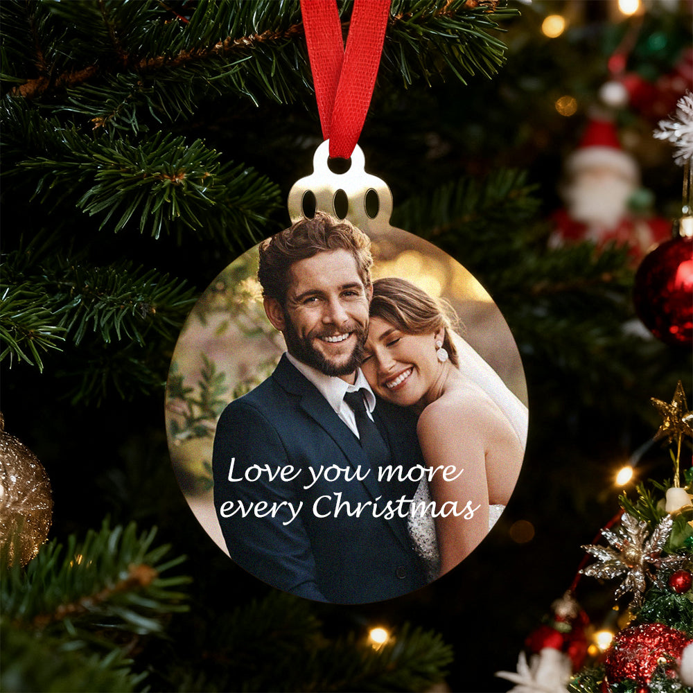 Personalized Christmas ornament with a couple's photo and 'Love you more every Christmas' text, hanging on a decorated tree.