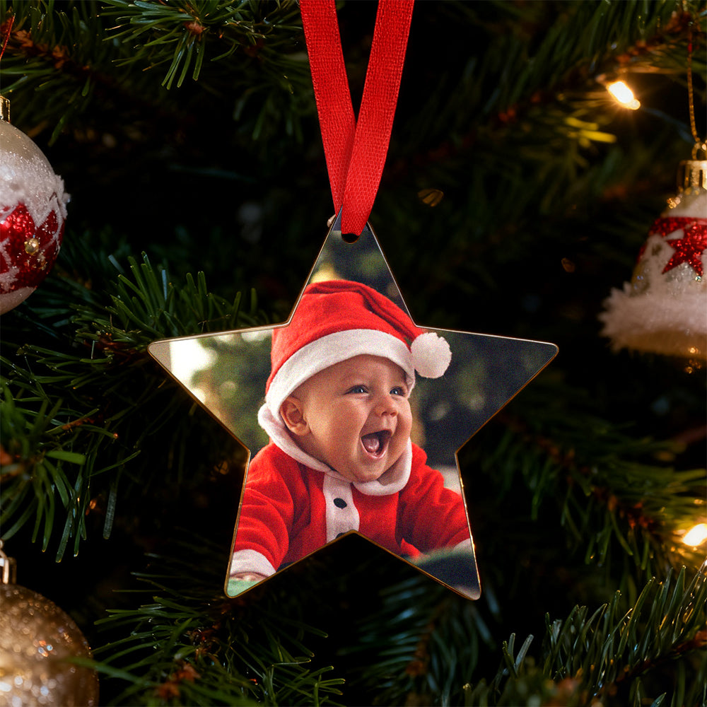Star-shaped Christmas ornament with a baby in a Santa outfit on a tree.