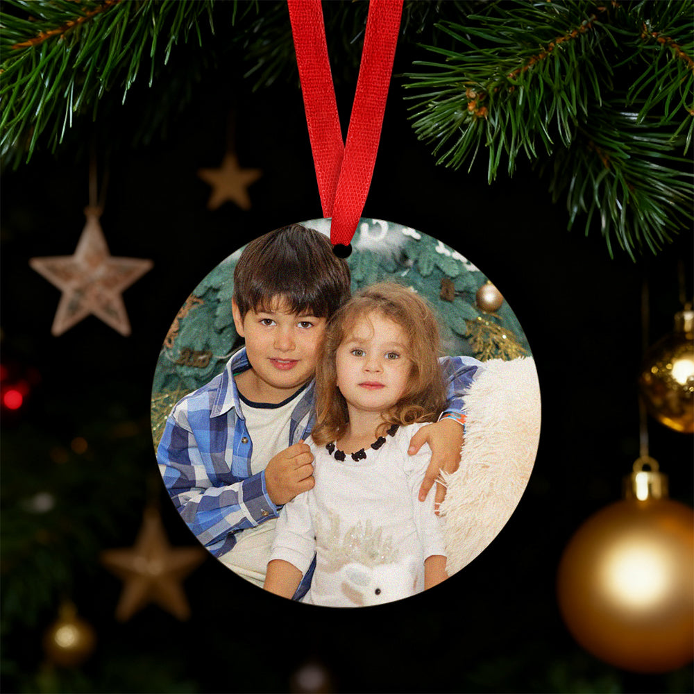 Round photo ornament with two children on a Christmas tree.