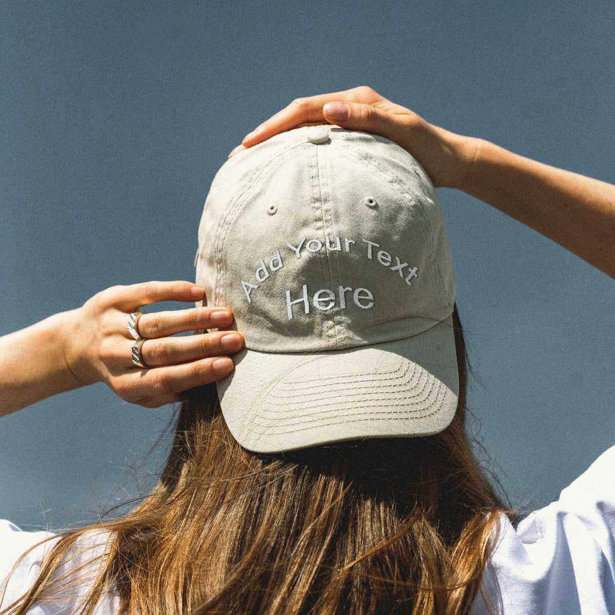 Women holding a beige cap with 'Add Your Text Here' text