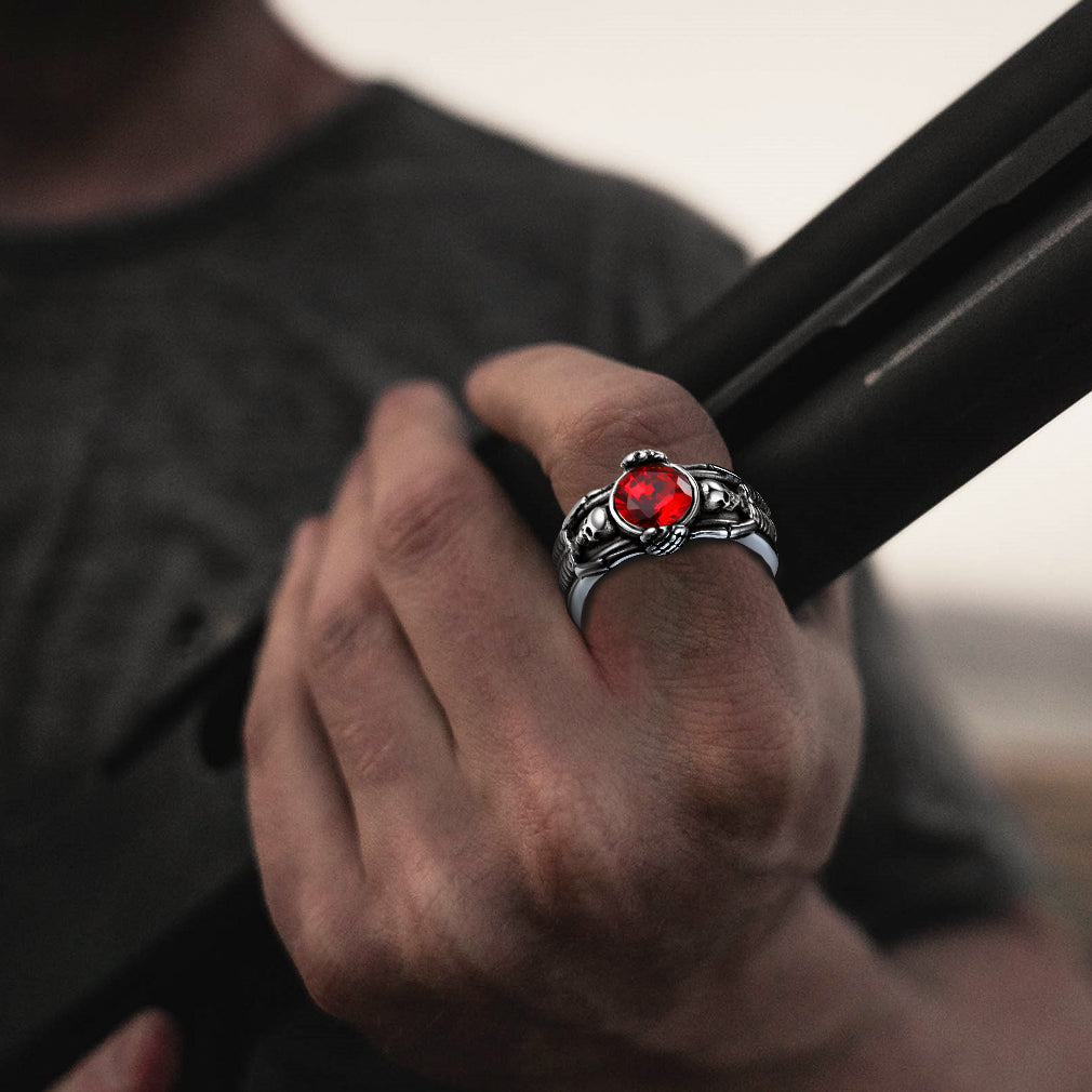 Hand wearing a silver ring with a red gemstone, holding a black object.