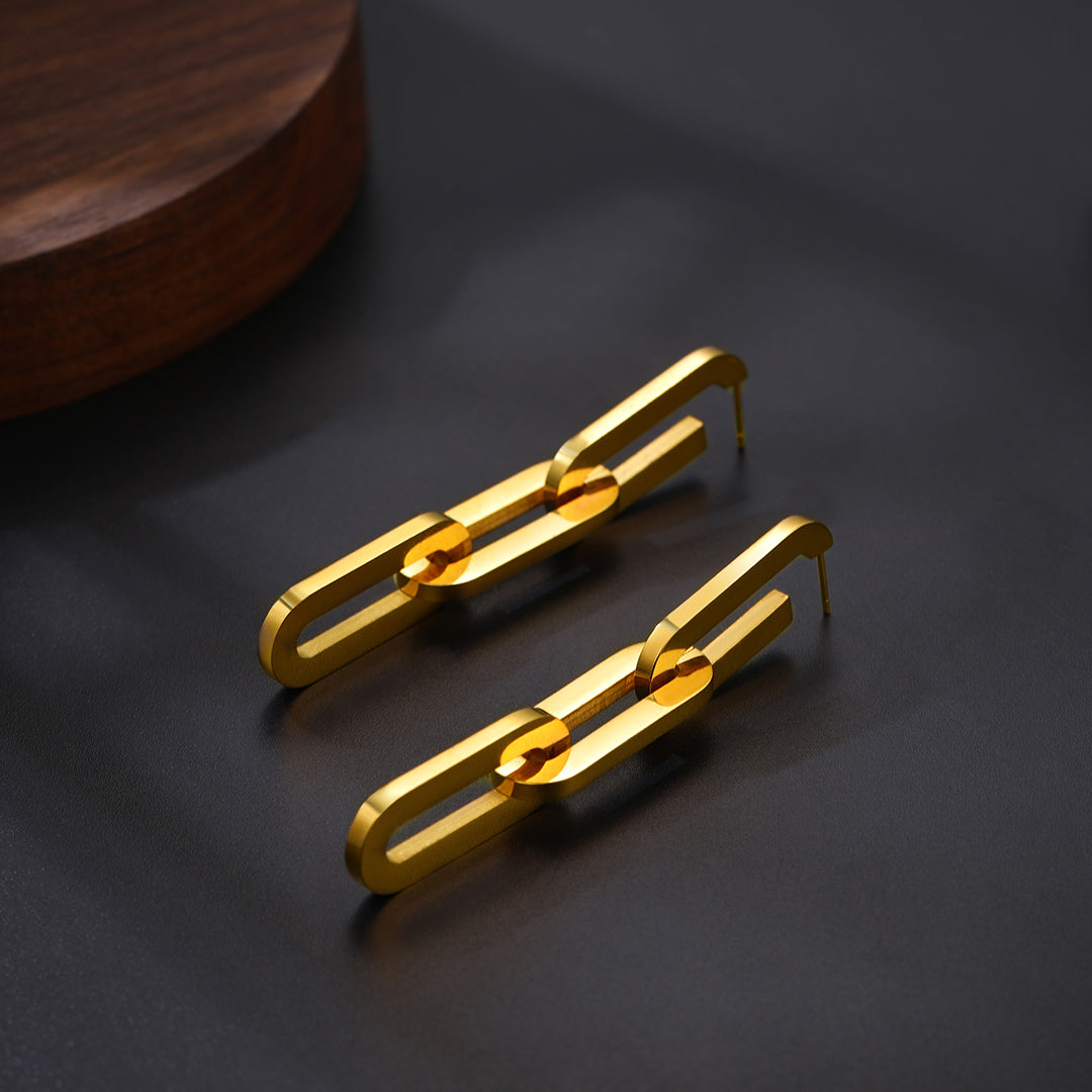 Gold chain-style earrings on a dark surface with a wooden object in the background