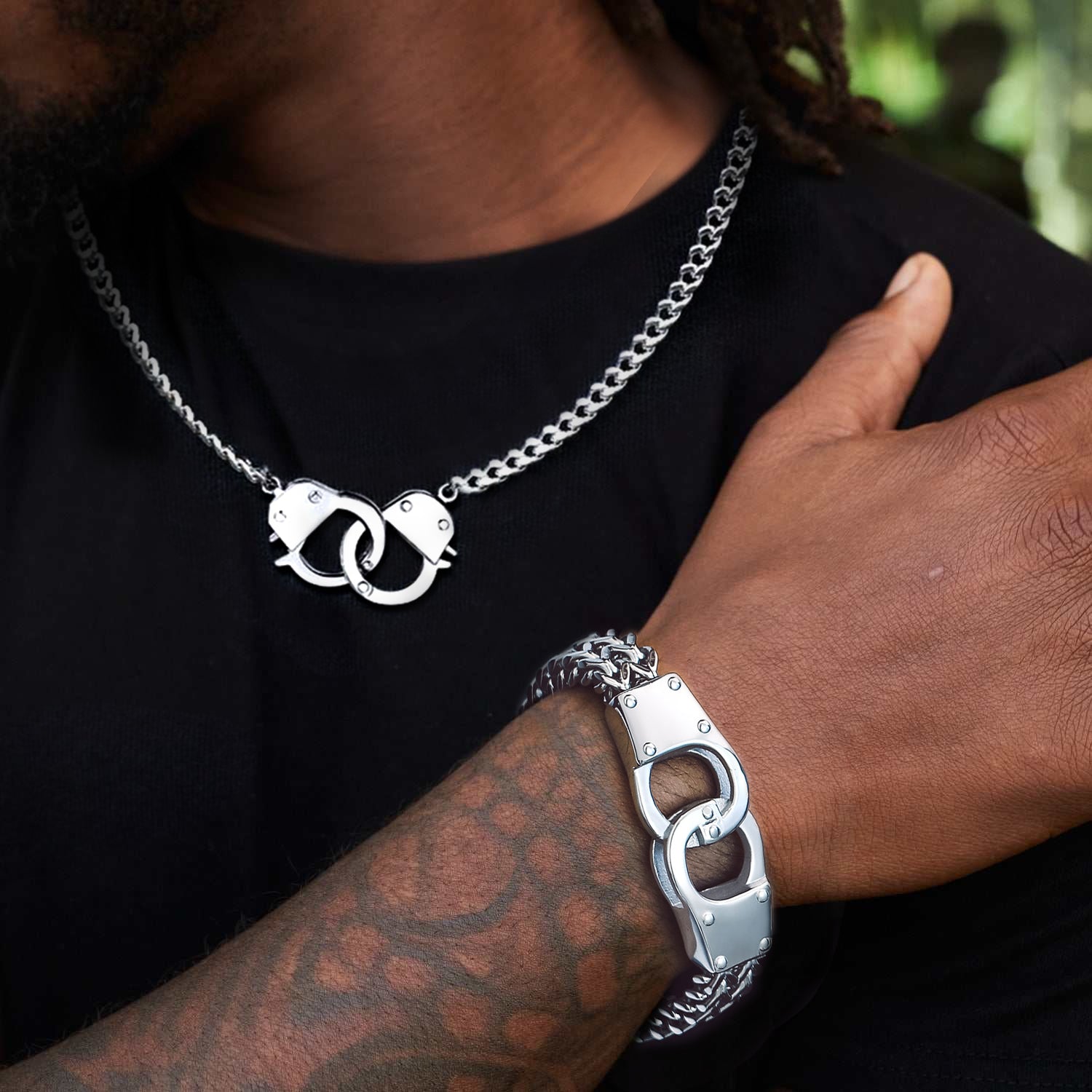 Person wearing a silver necklace and bracelet with intricate designs, set against a blurred natural background.