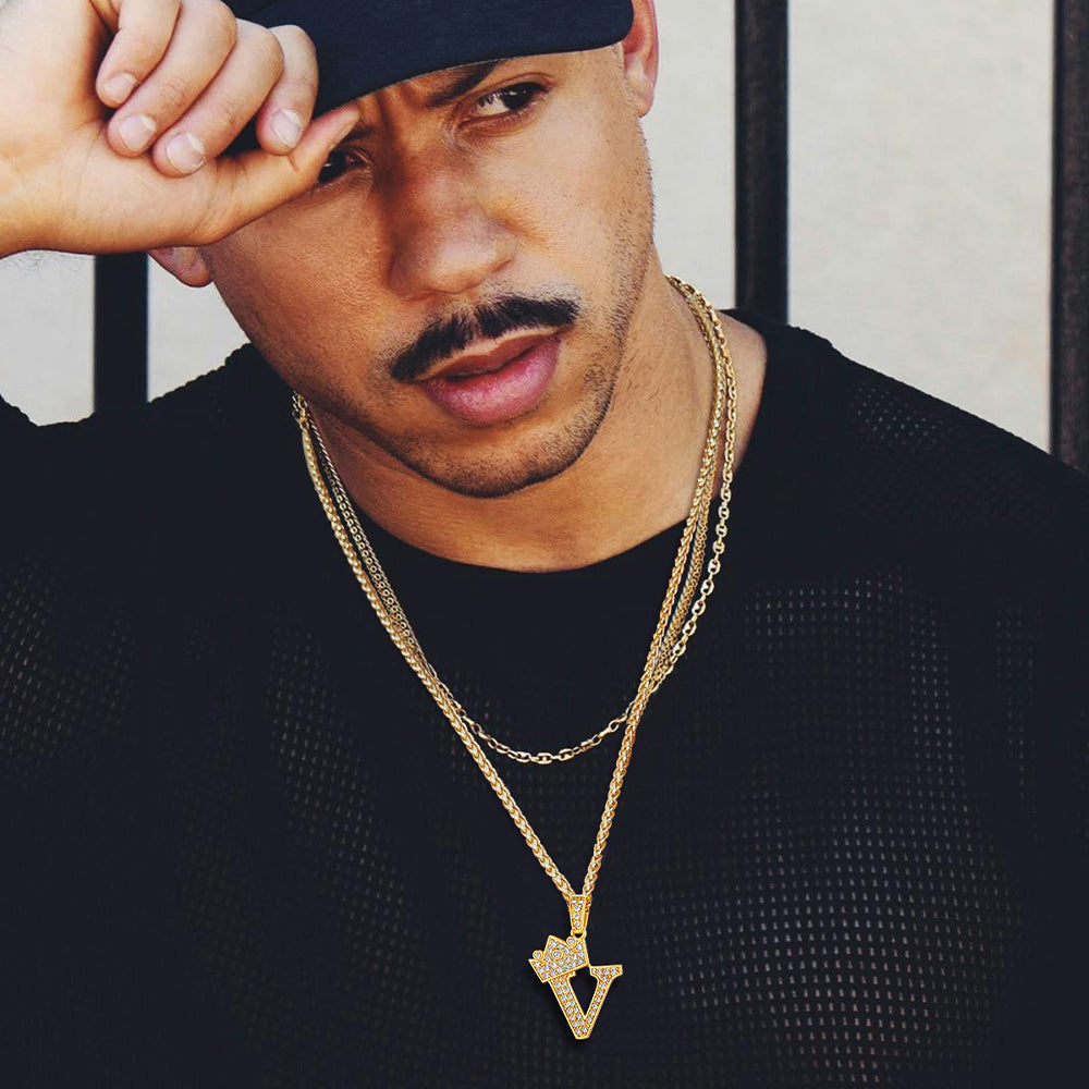 Man wearing a black sweater and gold necklace with a pendant, holding his hand to his forehead.