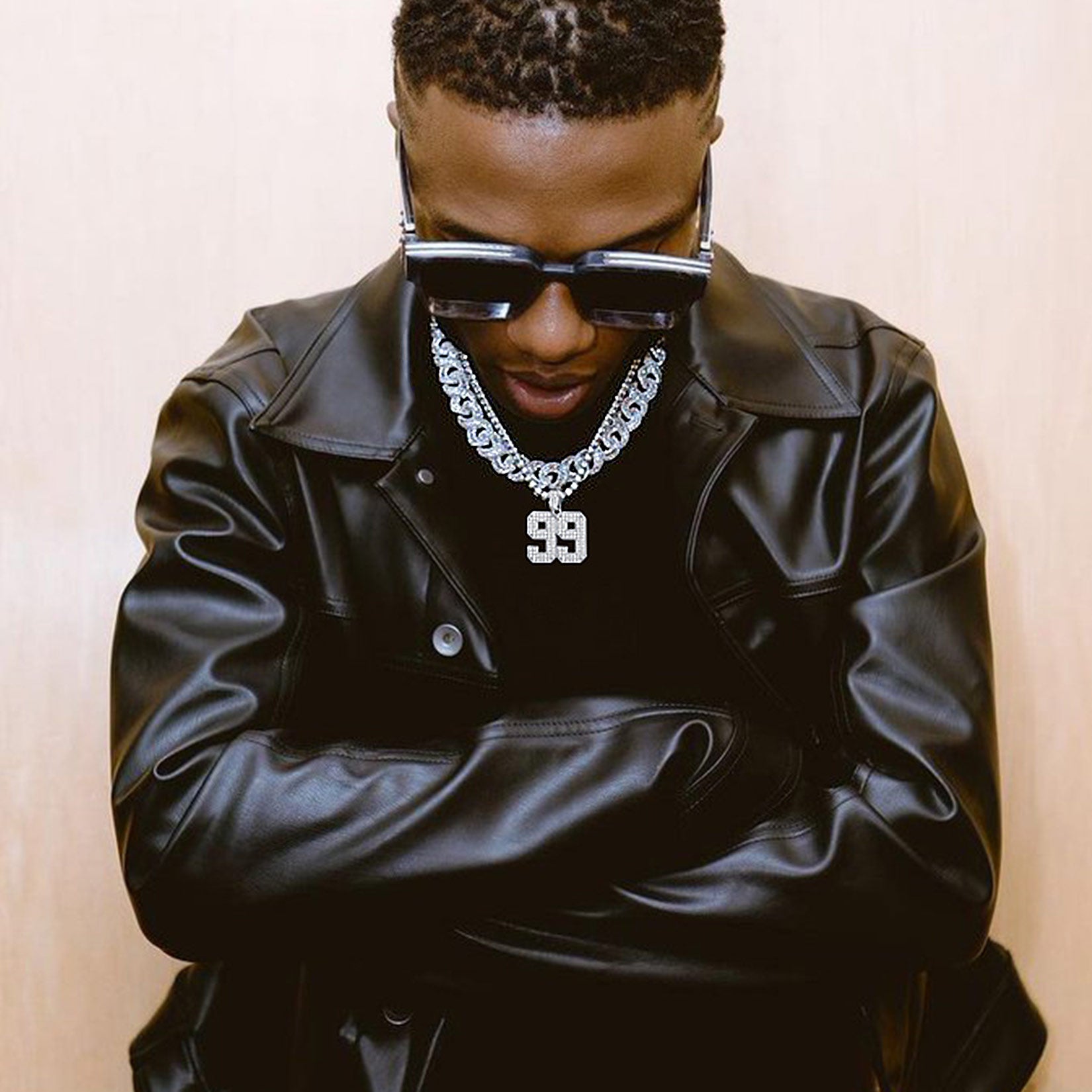 Person wearing a black leather jacket, sunglasses, and a chain necklace with a number '99' pendant.