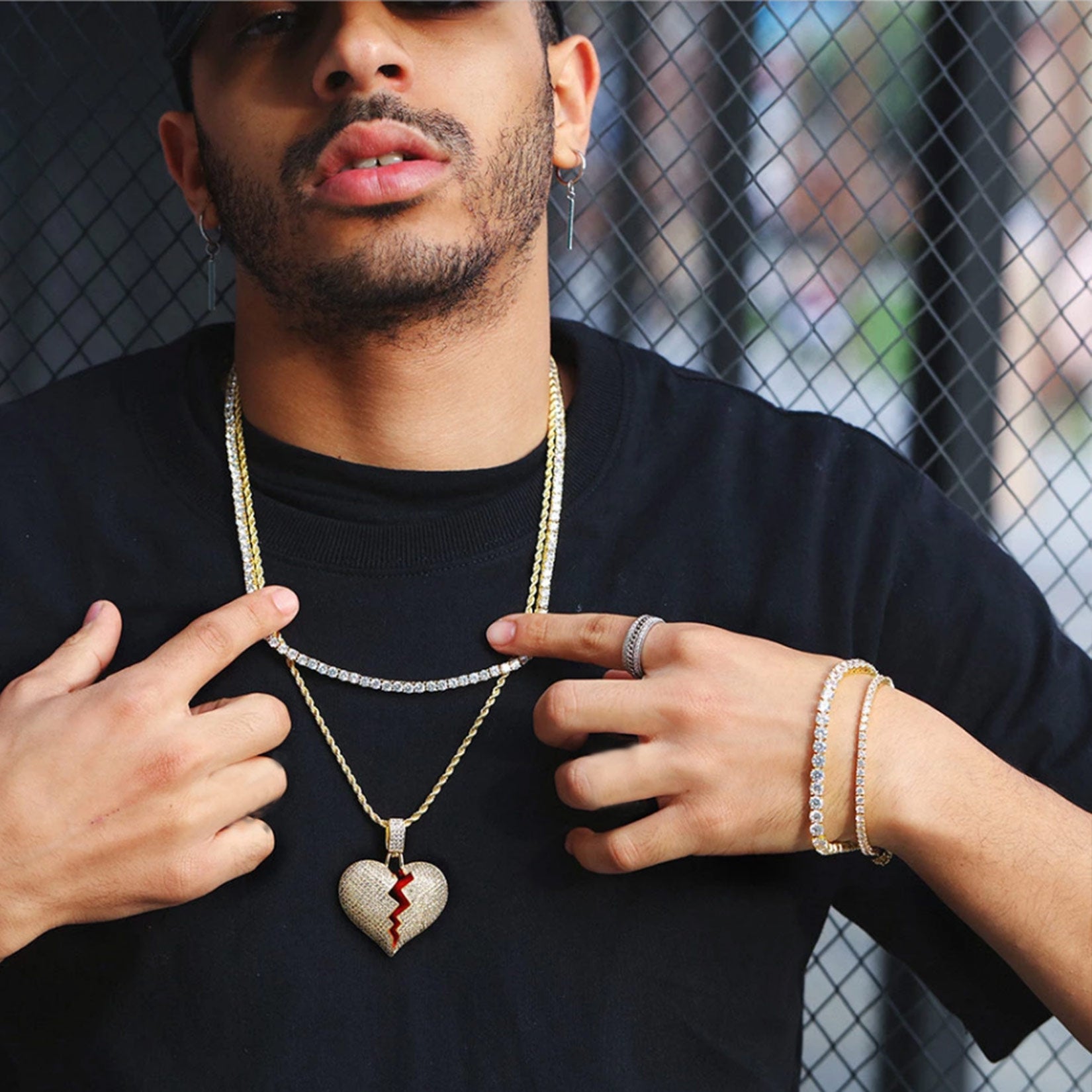 Man wearing a black shirt with jewelry including a necklace and heart-shaped pendant.