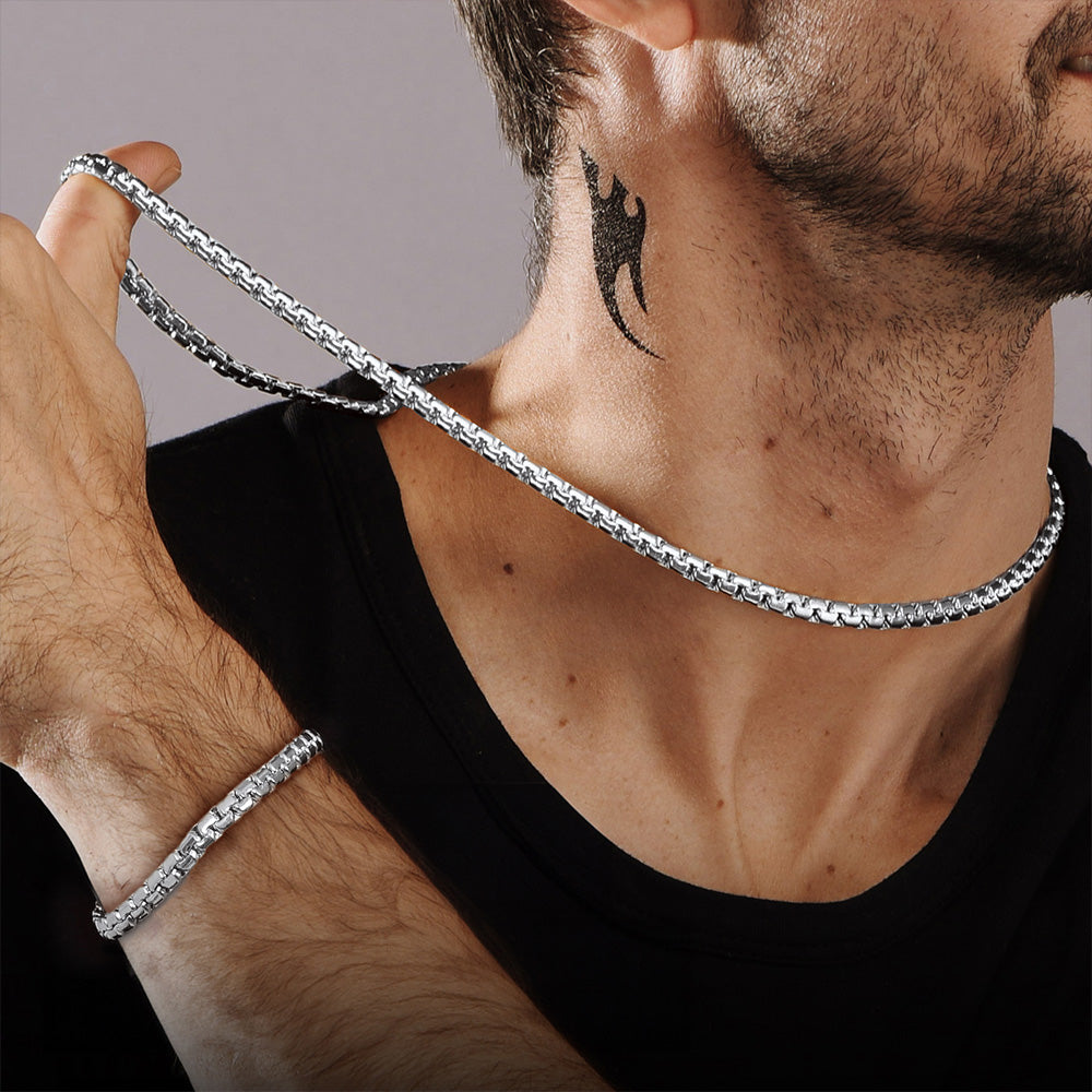 Man wearing a silver chain necklace and bracelet on a neutral background