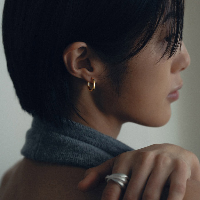 Close-up of a person wearing a gold earring and silver ring, with a neutral background.