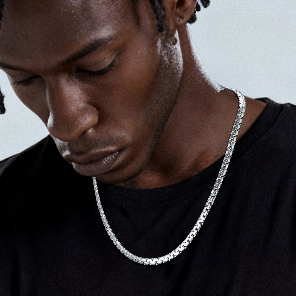 Man wearing a silver chain necklace against a neutral background