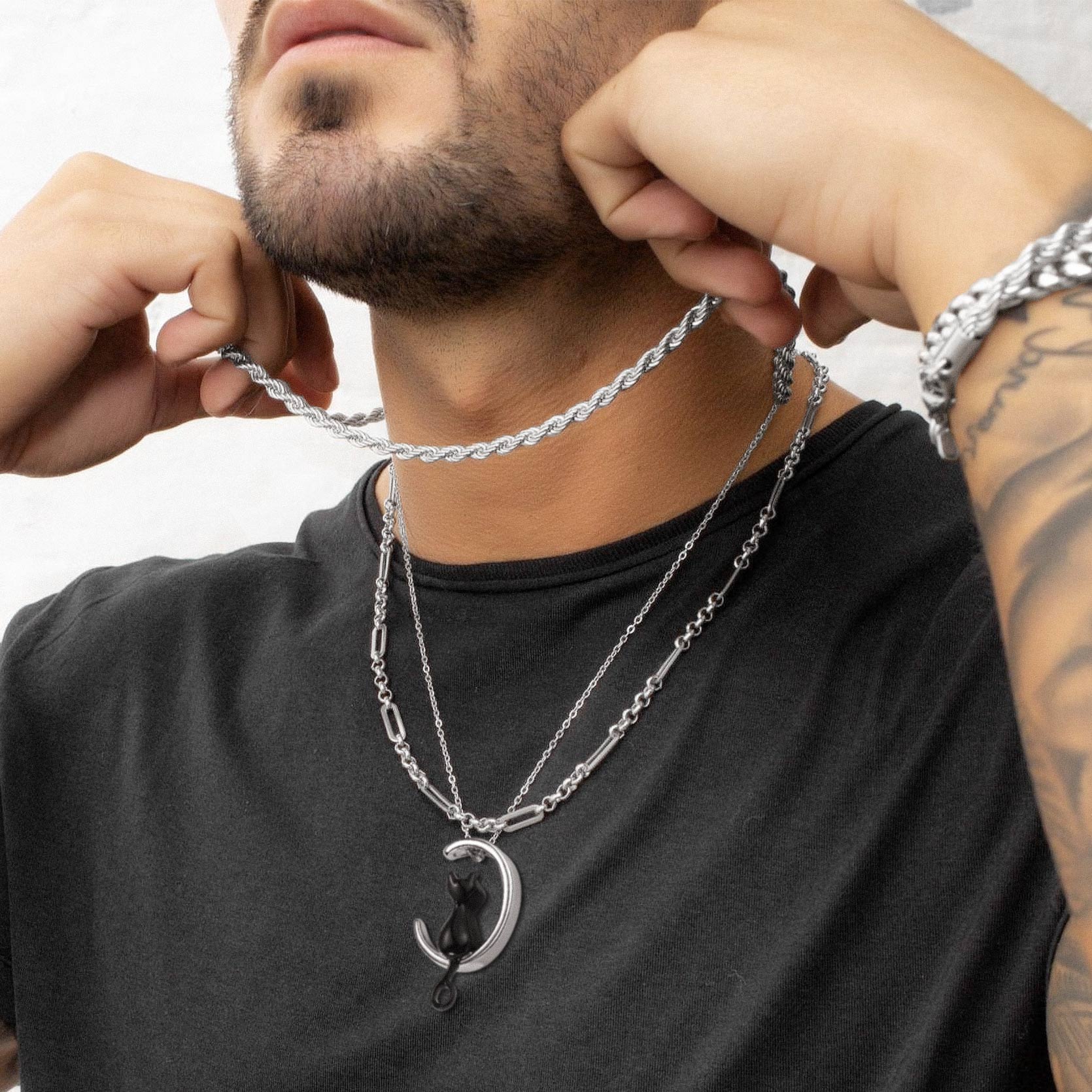 Man wearing a silver chain necklace with a crescent moon pendant on a plain background