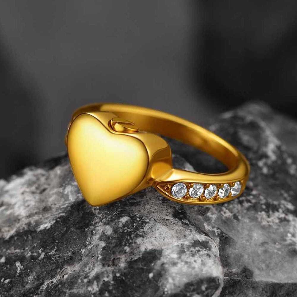 Gold heart-shaped ring with embedded stones on a dark stone surface