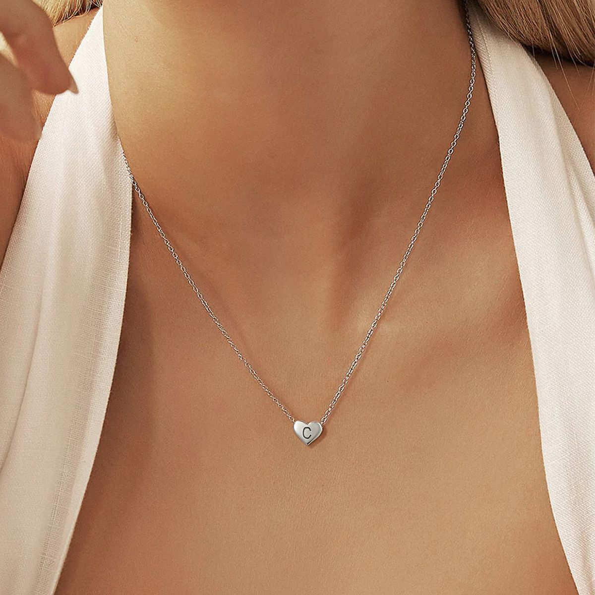 Silver necklace with a heart-shaped pendant on a person wearing a white top.