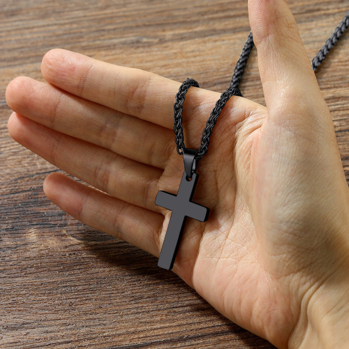 Hand holding a black cross necklace on a wooden surface