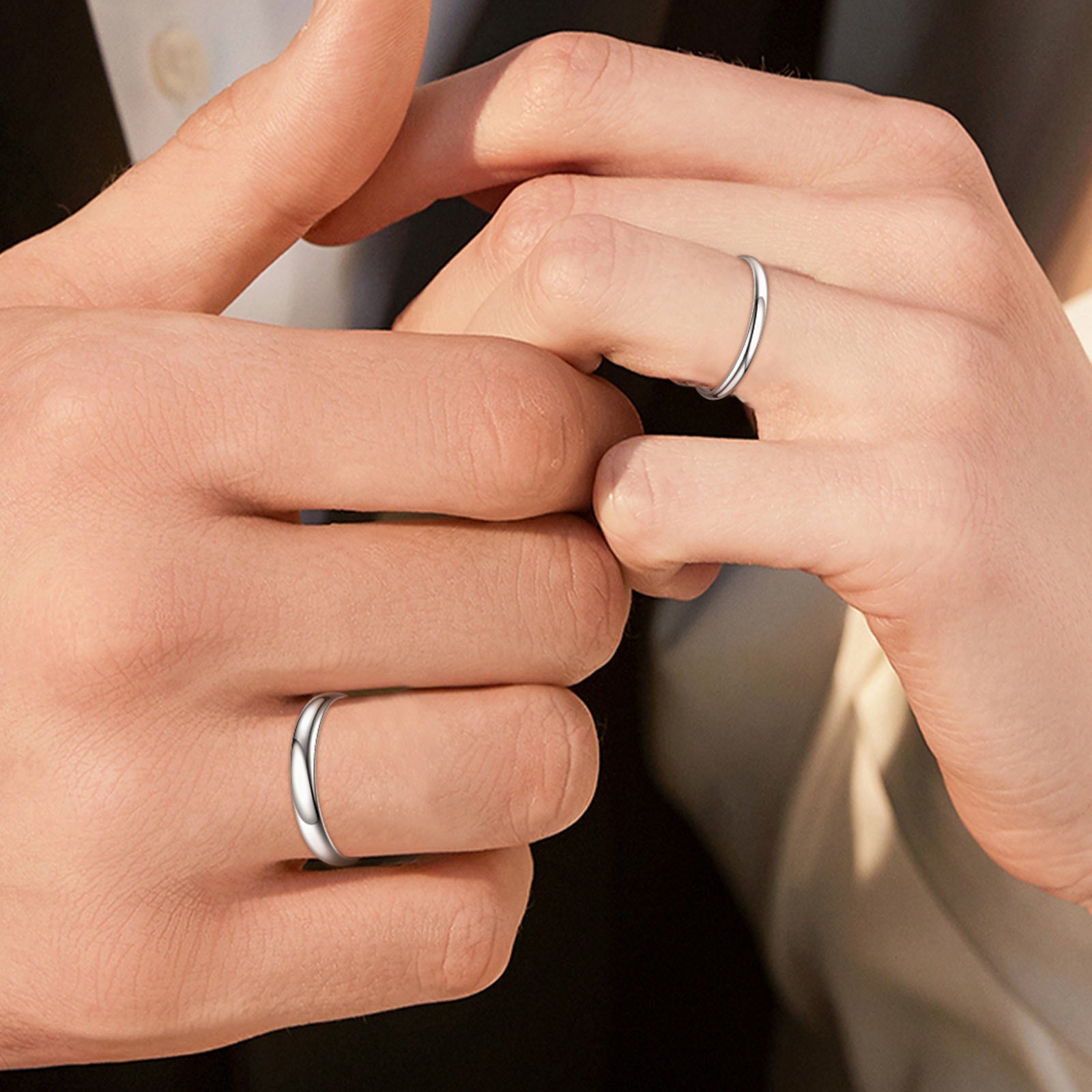 Close-up of two hands wearing silver rings on a neutral background