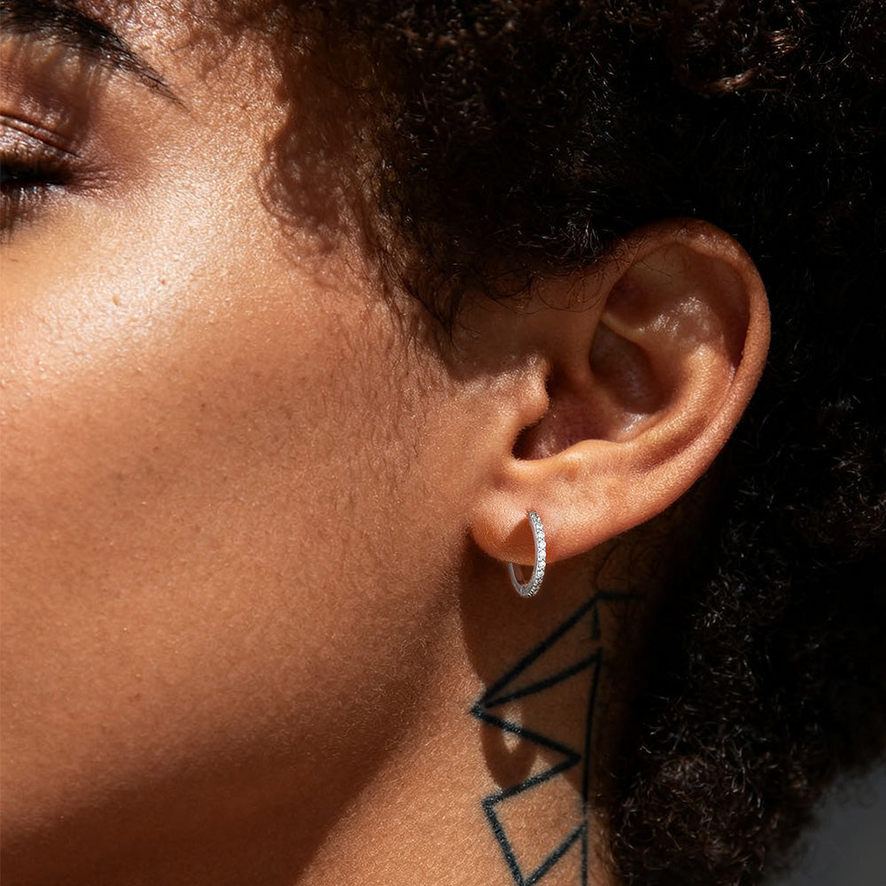 Close-up of a person wearing a silver hoop earring with a dark background