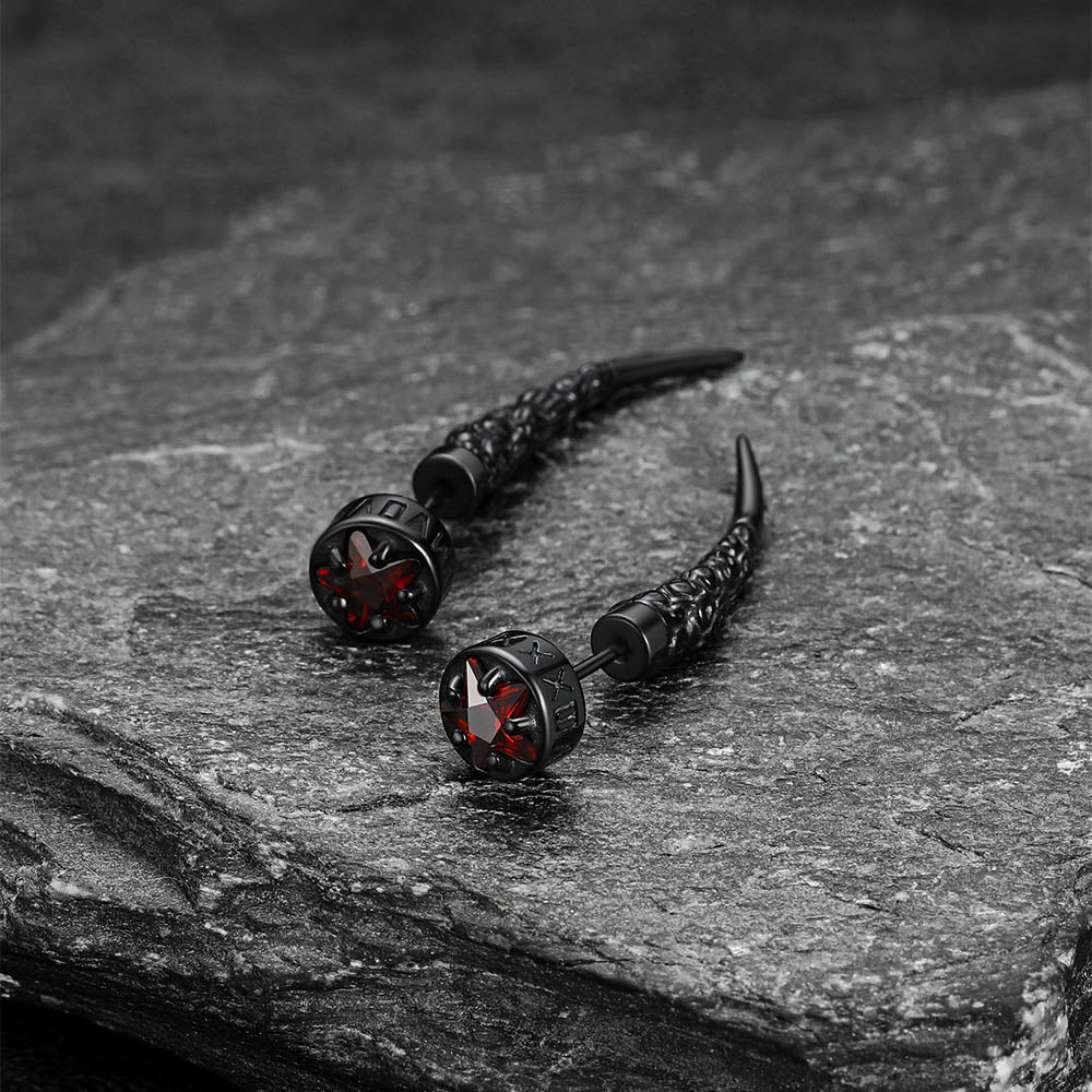 Pair of black earrings with red accents on a stone surface