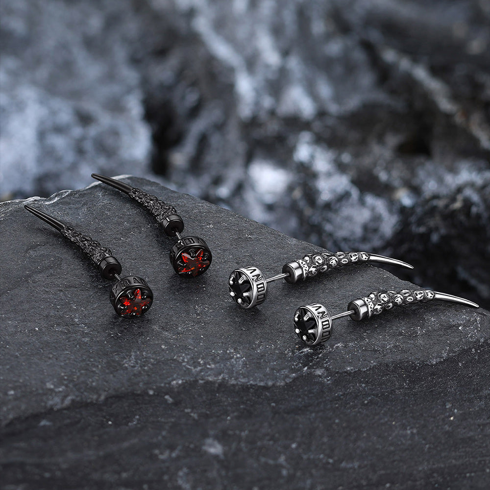 Pair of black and silver Viking Nordic Star Rune Fang Stud Earrings on a dark stone surface with a blurred natural background