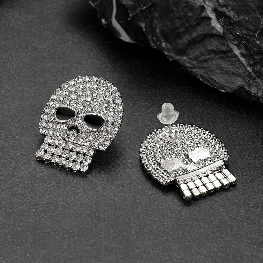 Silver skull-shaped earrings with clear stones on a dark surface