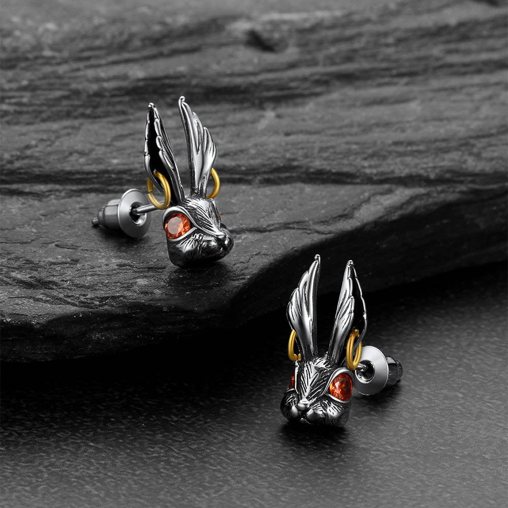 Silver rabbit-shaped earrings with red eyes on a dark stone surface