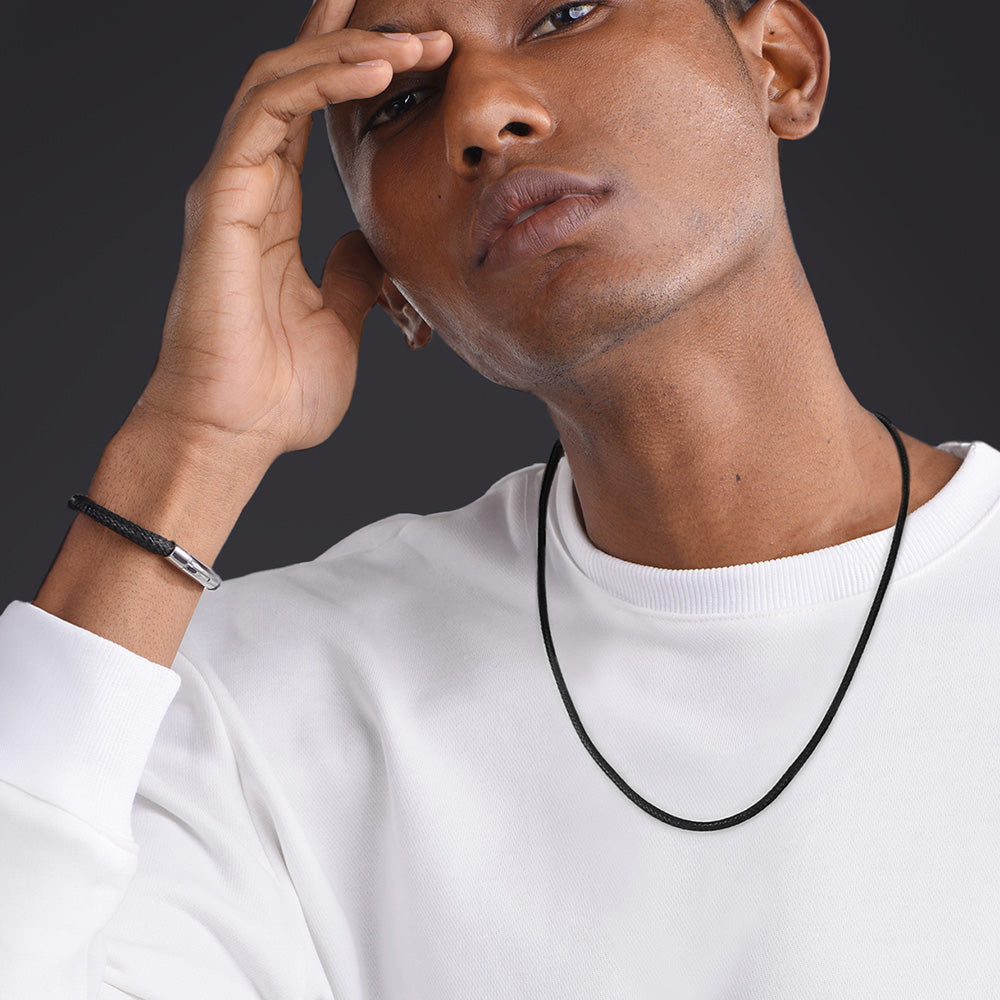 Man wearing a white shirt and black necklace against a dark background
