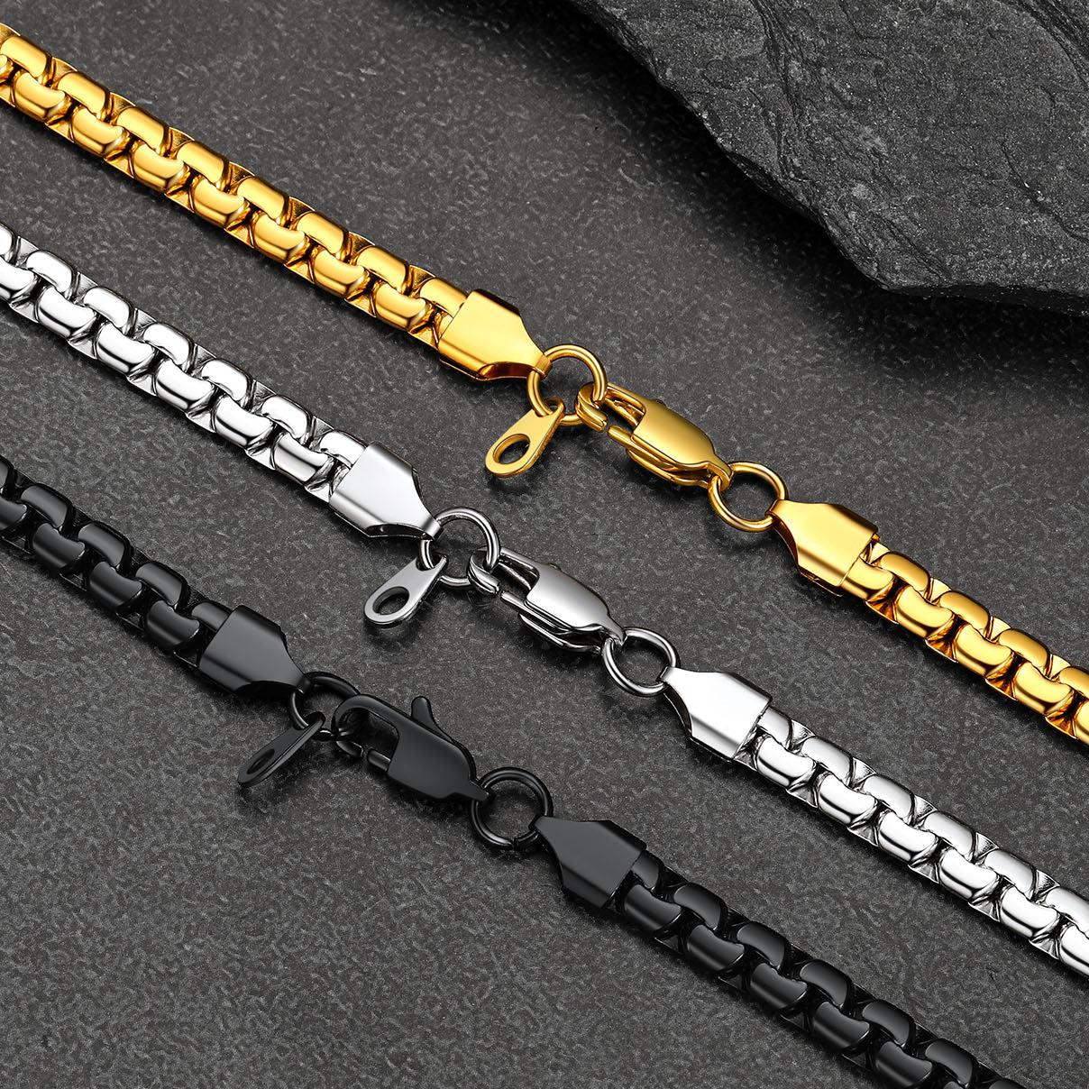 Three gold, silver, and black chain necklaces on a dark stone surface.