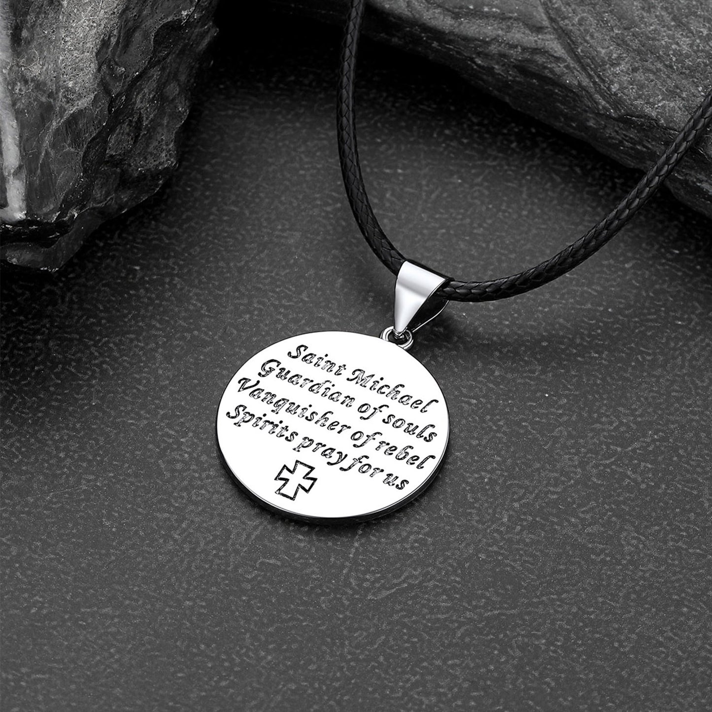 Silver pendant with engraved text on a black cord against a dark stone background
