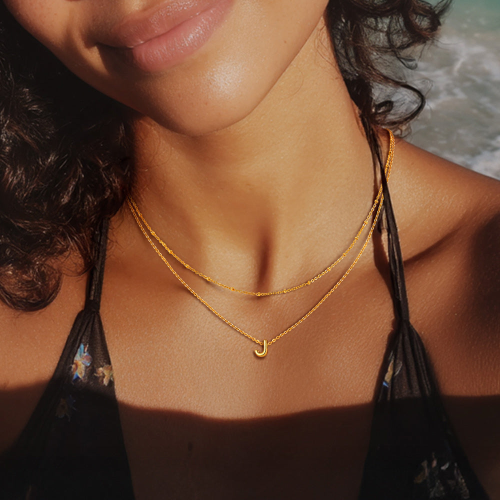 Female model styling silver A-Z charm necklace with minimalist white blouse