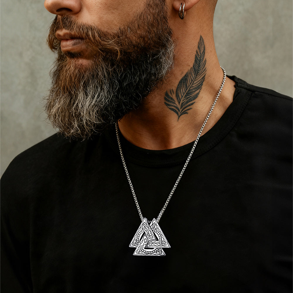 Man wearing a black shirt with a silver necklace featuring a triangular pendant.