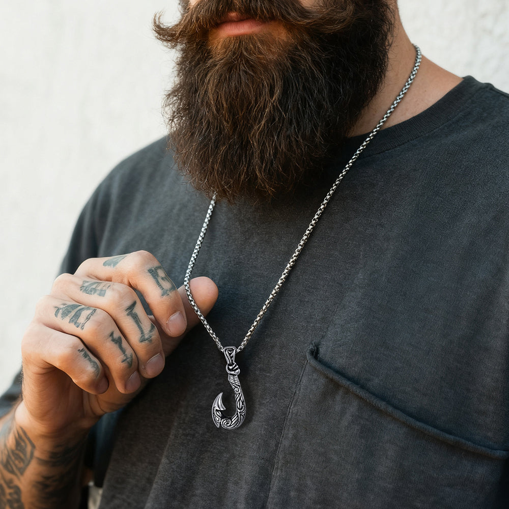 Man wearing a dark gray shirt with a necklace featuring a hook pendant.