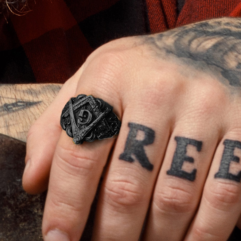 Hand wearing a black ring with a symbol, with tattoos on the fingers.