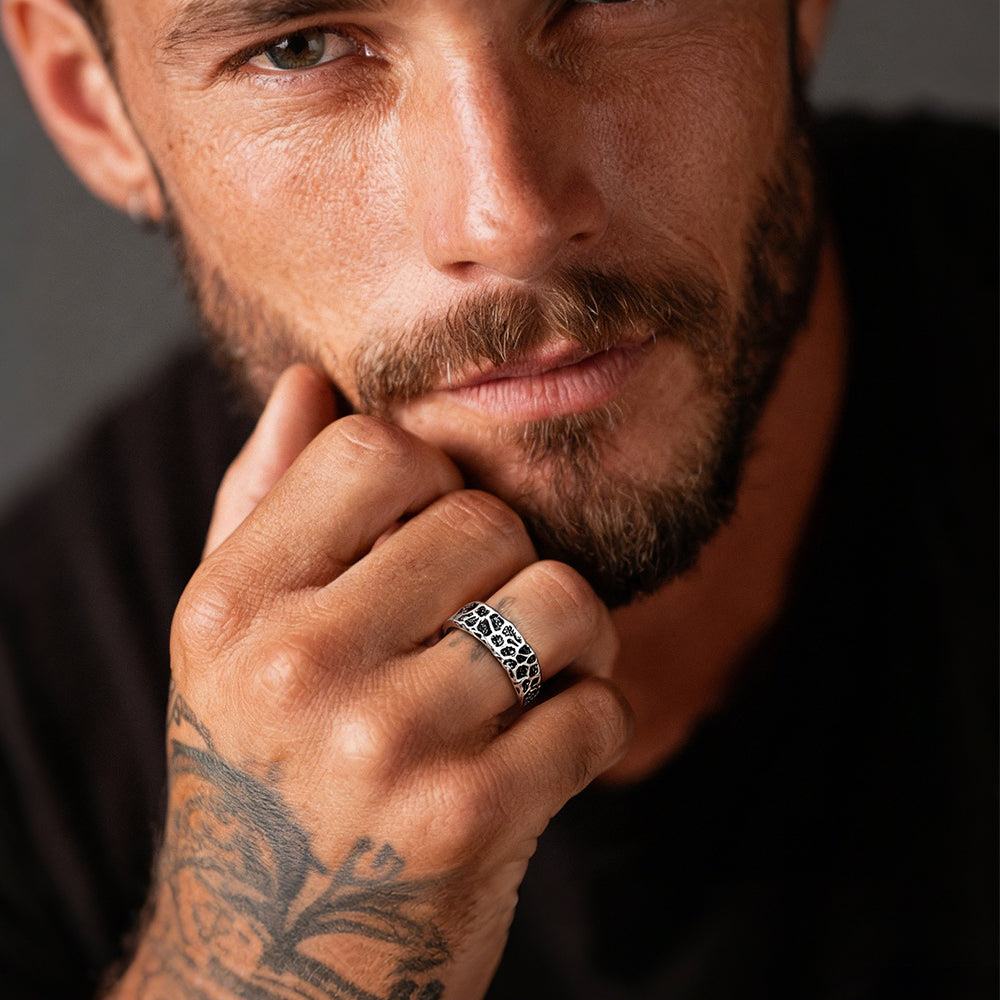 Man with tattoos and a ring on his finger against a dark background