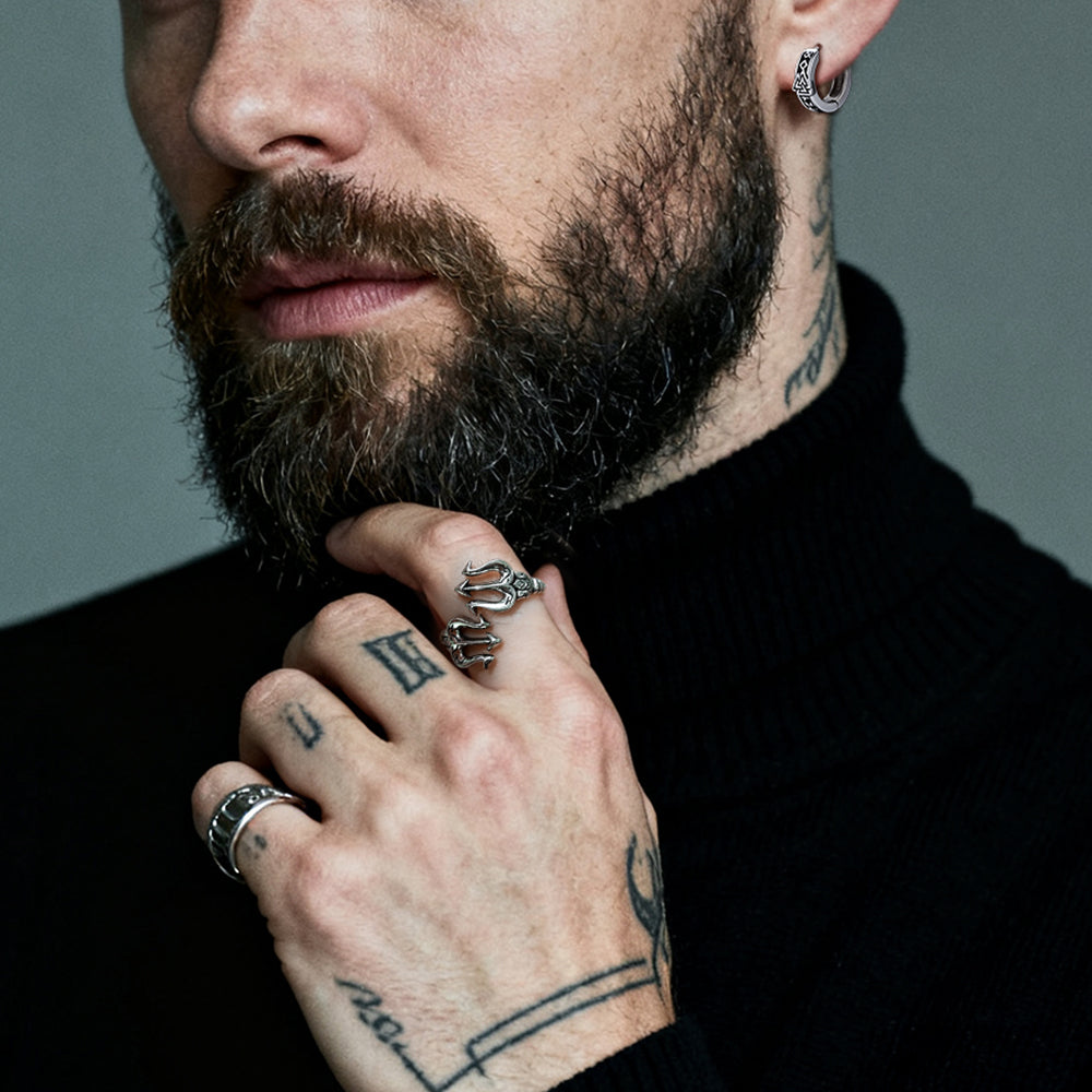 Man with tattoos wearing Poseidon Trident Ring on his fingers against a gray background