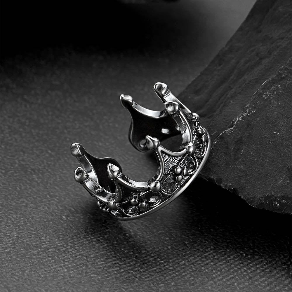 Silver crown-shaped earring on a dark textured surface