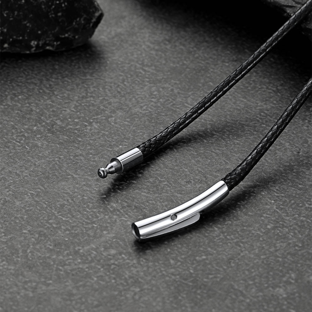 Close-up of a black braided cord with metal clasp on a dark surface