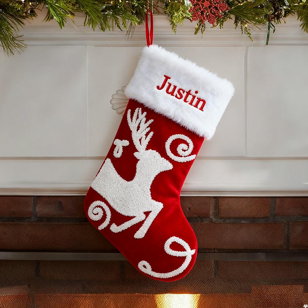 Red Christmas stocking with white reindeer design and 'Justin' embroidery, hanging on a fireplace.