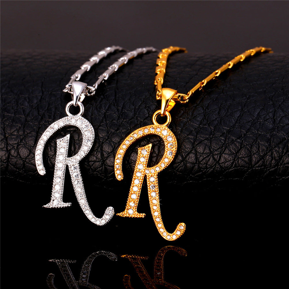 Two gold and silver necklaces with 'R' pendants on a dark surface.