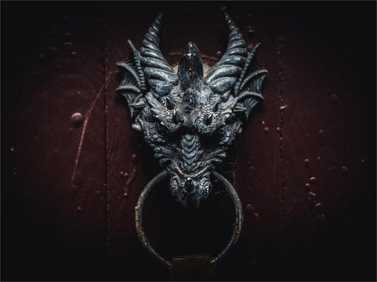 A close-up of a gothic dragon head door knocker on a dark red wooden door