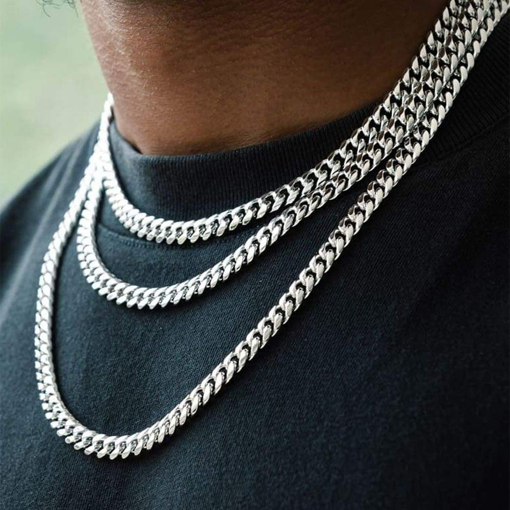 Close-up of a person wearing 3silver chain necklaces on a dark shirt.