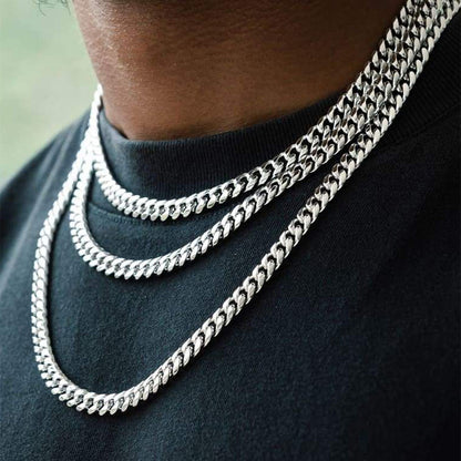 Close-up of a person wearing 3silver chain necklaces on a dark shirt.