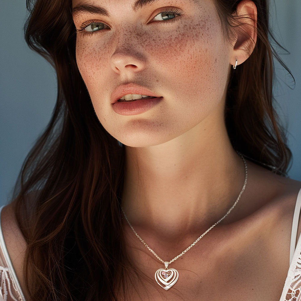 Close-up of a woman wearing a silver necklace with a heart pendant against a light blue background