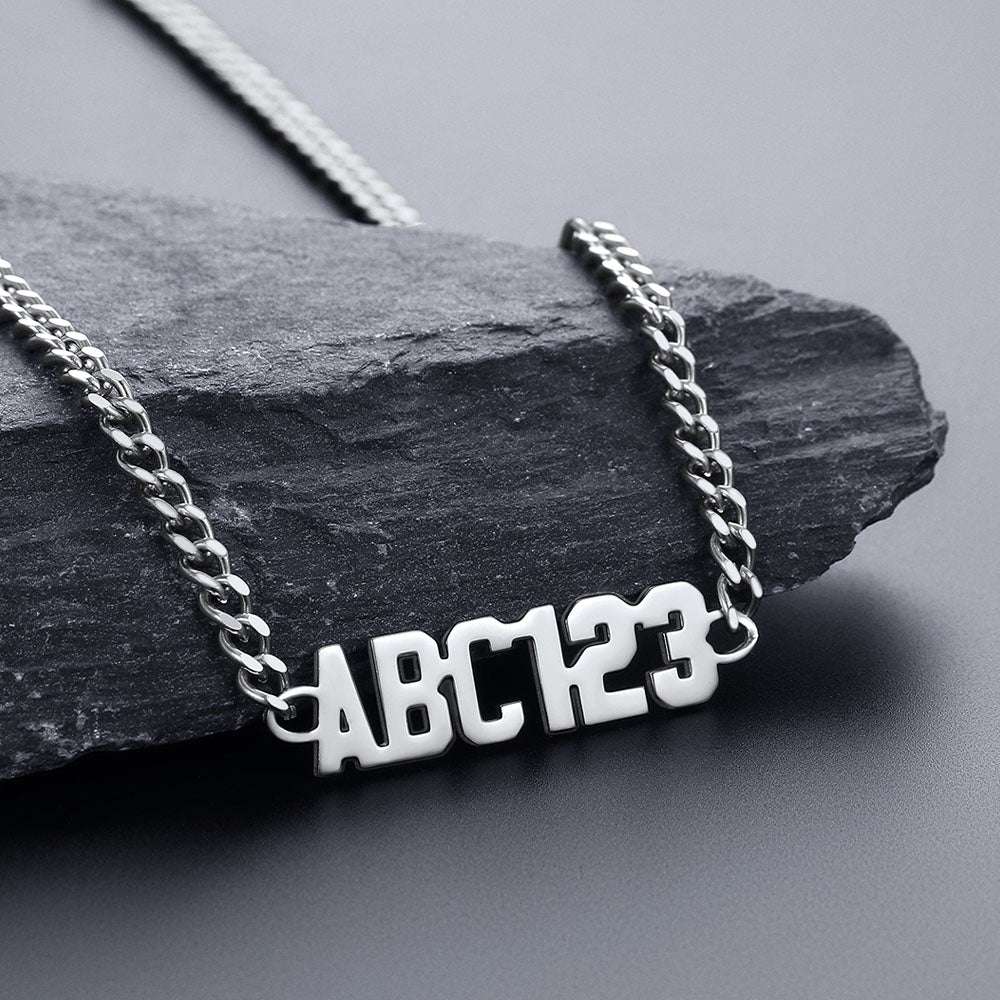 Silver necklace with 'ABC123' pendant on a dark stone surface